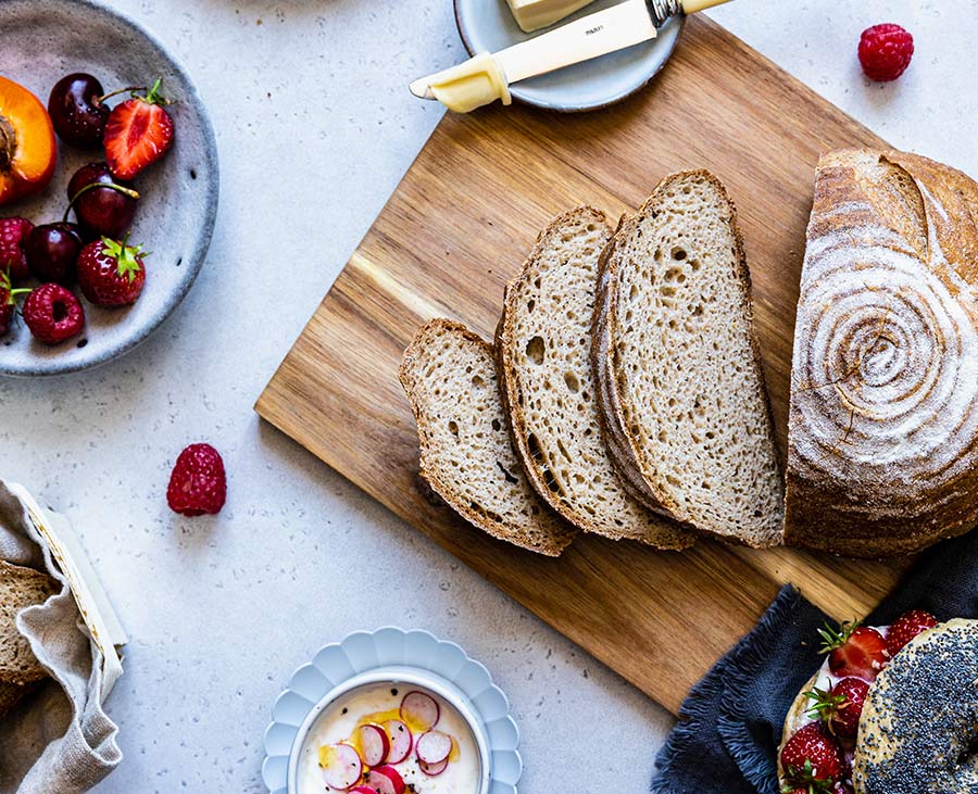 Pain Piaf sans gluten coupé en tranches sur une planche en bois avec quelques fruits rouges.